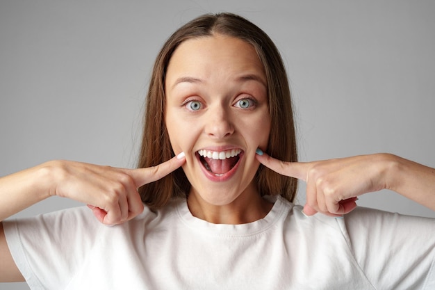 picture of beautiful young woman smiling and pointing to teeth on gray background