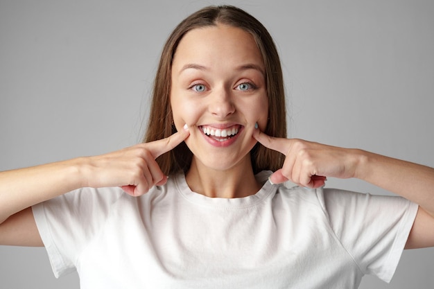 picture of beautiful young woman smiling and pointing to teeth on gray background
