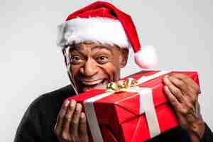 Photo a picture of a black man wearing a santa hat and holding a gift box in a white studio