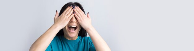 Picture of brunette teenage girl covering face with hands and peeping through her fingers.