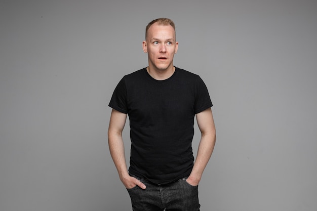 Photo picture of caucasian man keeps his hands in the pockets of his black jeans and looks to the right isolated on grey background