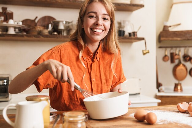 キッチンで料理をしている陽気な若いブロンドの女の子のシェフの写真。