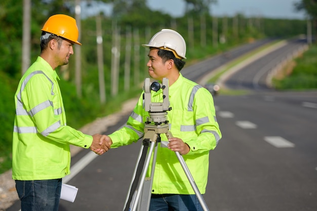 Immagine di un ingegnere civile e di un ingegnere di rilevamento che misura con un teodolite. il teodolite viene utilizzato per misurare le coordinate del terreno. la stretta di mano all'aperto è benvenuta nei cantieri stradali.