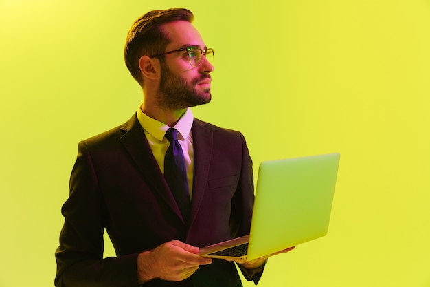 Picture of a concentrated young business man posing isolated over light green wall wall with led neon lights using laptop computer.