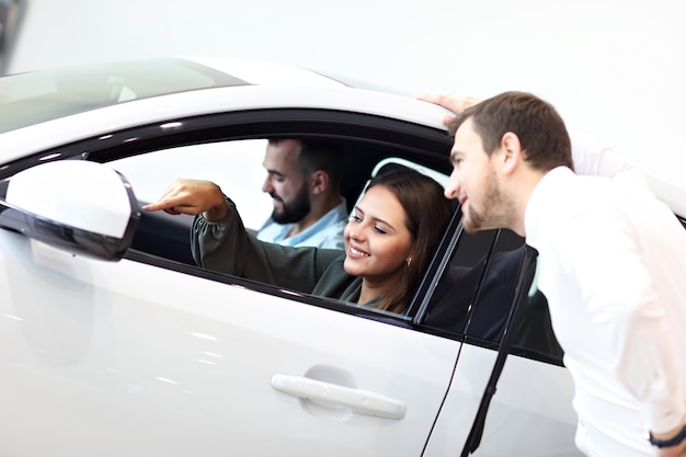 Picture of confident young salesman explaining all the car features to the young attractive owners