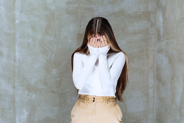 Picture of a cute girl model standing and closing face with hands 