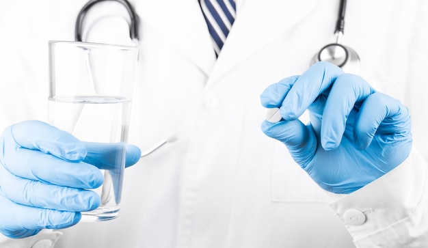 白い丸薬とコップ一杯の水を与える医者の手の写真