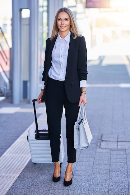 Immagine di una donna elegante che cammina con borsa e valigia nella stazione ferroviaria