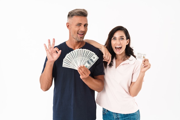 Picture of emotional surprised adult loving couple isolated over white wall holding money and credit card.