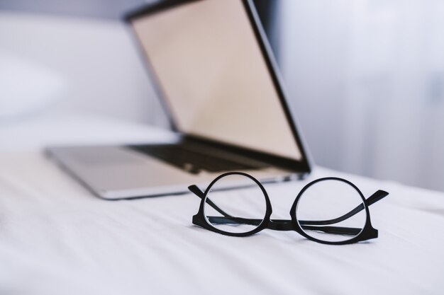 Photo picture of eyeglasses and laptop on bed in bedroom
