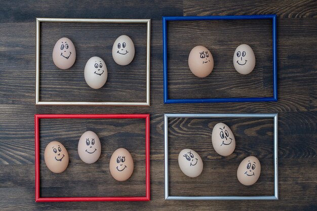 Picture frame and many funny eggs smiling on dark wooden wall background, close up. Eggs family emotion face portrait. Concept funny food