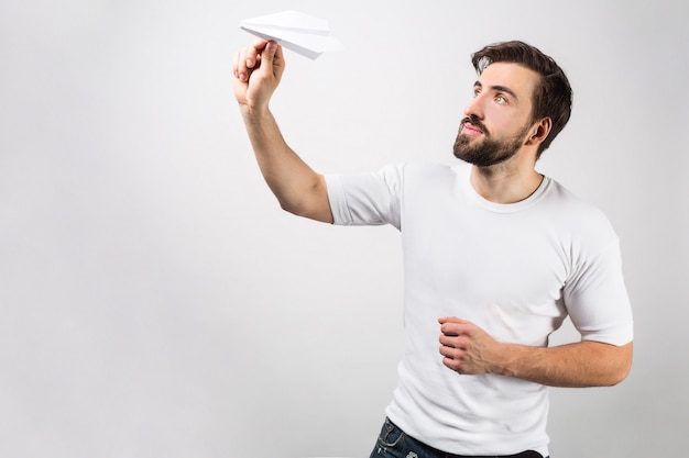 白いシャツを着た男が紙飛行機を洗う準備ができている別の角度からの写真。彼は何でもできます。白い壁に分離されました。