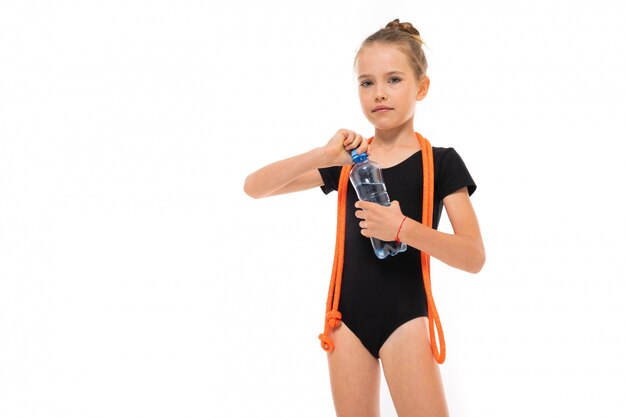 Foto di ragazza ginnasta in trico nero in piena altezza con una corda per saltare al collo e una bottiglia di acqua in mano isolato su uno sfondo bianco