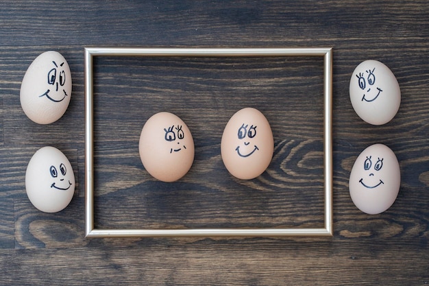 Picture golden frame and many funny eggs smiling on dark wooden wall background Eggs family emotion face portrait Concept funny food