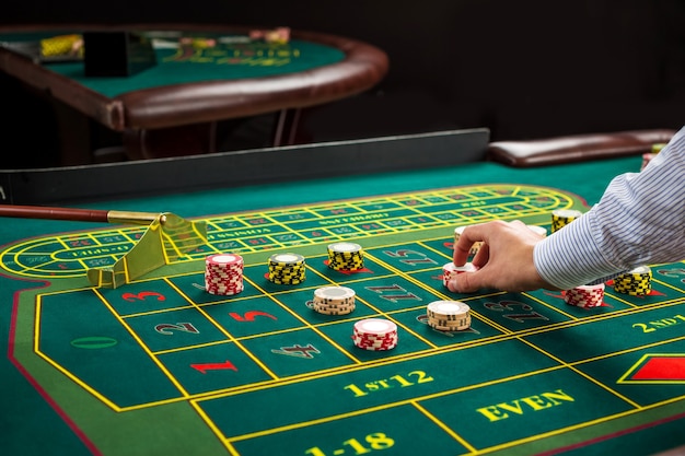 Picture of a green table and betting with chips. Man hand over casino chips on roulette table. Close up