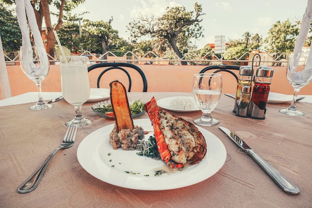 Picture grilled lobster with fresh tomato and cucumber on white plate rice and a cocktail glass on the tablecloth Beautiful expensive dinner in a street restaurant on the background of city