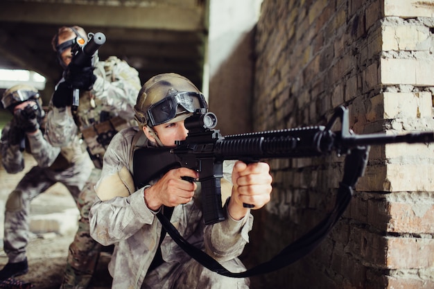 A picture of guy looking for an aim. He is loooking through loop gun. He is concentrated. There are two people with rifles standing behind them. They are also taking aim.