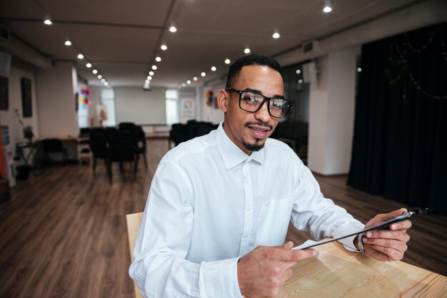 Picture of handsome businessman wearing glasses sitting at the table and looking at front