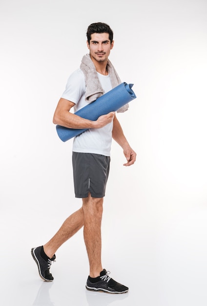 Picture of handsome sportsman with towel in gym standing over white wall.