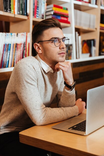 Picture of handsome young man wearing eyeglasses sitting in cafe while using laptop computer.