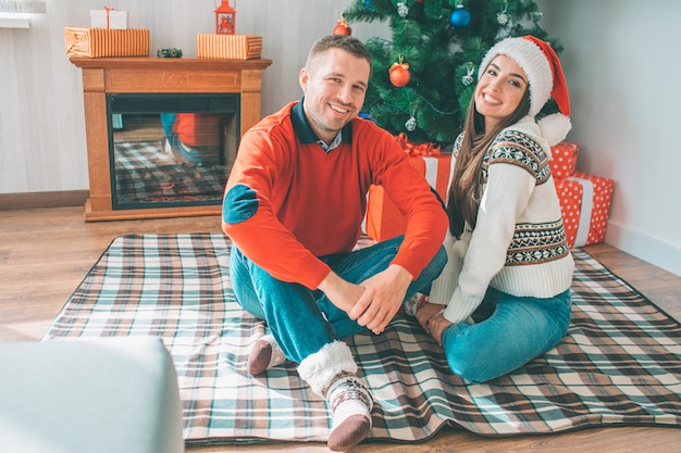 Picture of happy young couple sitting together on blanket. They smile and look at camera. 