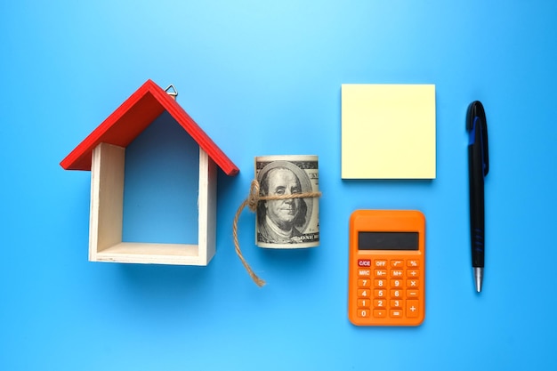 A picture house miniature with fake money notepad calculator on blue background