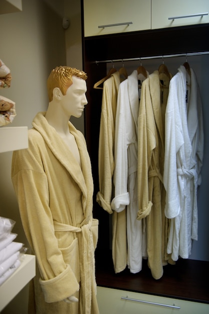 A picture of a lot of dressing gowns on wooden hangers in a store and a male mannequin in a dressing