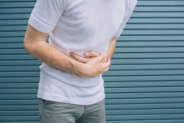 A picture of man's body. Guy is standing and holding hands on stomack. He feels bad.