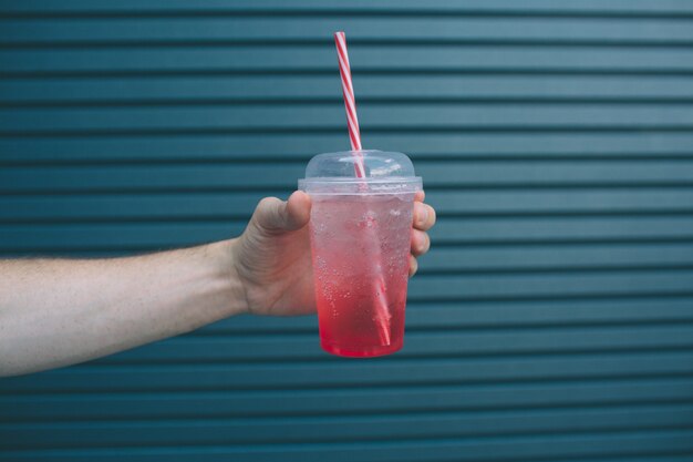 A picture of man's hand holding cup of red lemonade in hand. Isolated on striped 