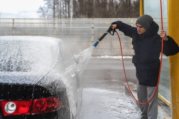 Фотография мужчины, моющего машину под высоким напором воды на улице в холодное время года.