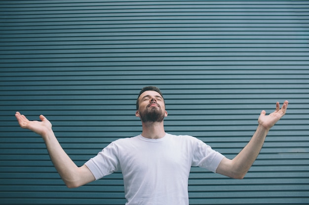 A picture of man in white shirt standing and holding hands on different sides. He is looking up. Guy is keeping eyes closed. He is praying. Isolated on striped 