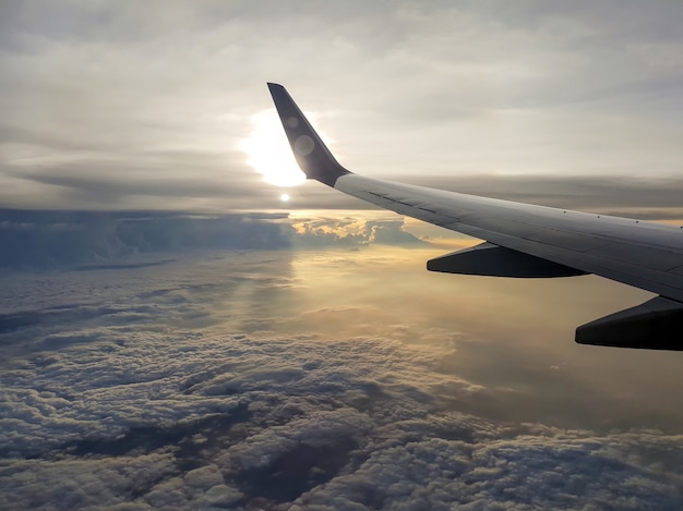 写真 朝の窓から太陽と雲の上空を飛行する飛行機の翼の写真