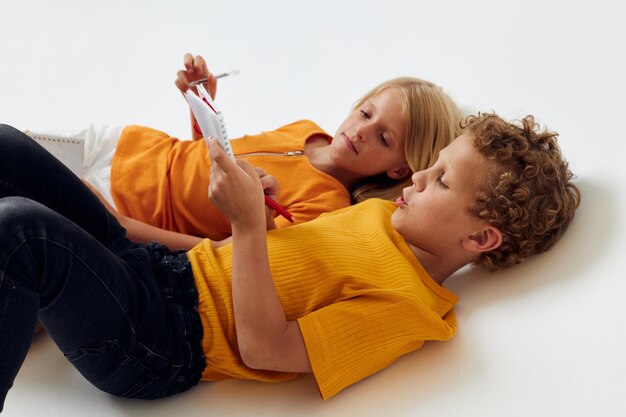 picture of positive boy and girl lie on the floor with notepads and pencils isolated background unaltered. High quality photo