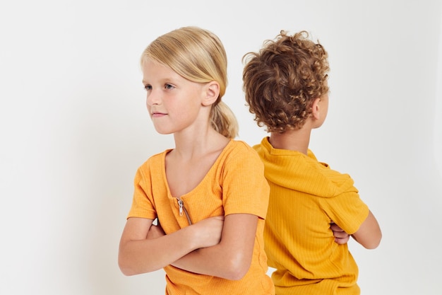 黄色のTシャツを着たポジティブな男の子と女の子が子供時代の感情を変えずに並べて立っている写真