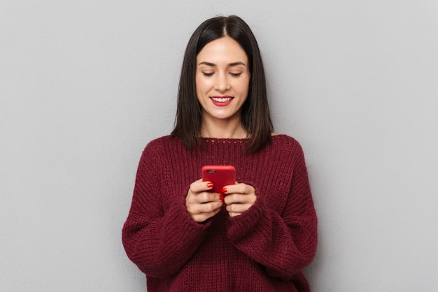 Foto di bella giovane donna vestita di maglione bordeaux utilizzando il telefono cellulare isolato.