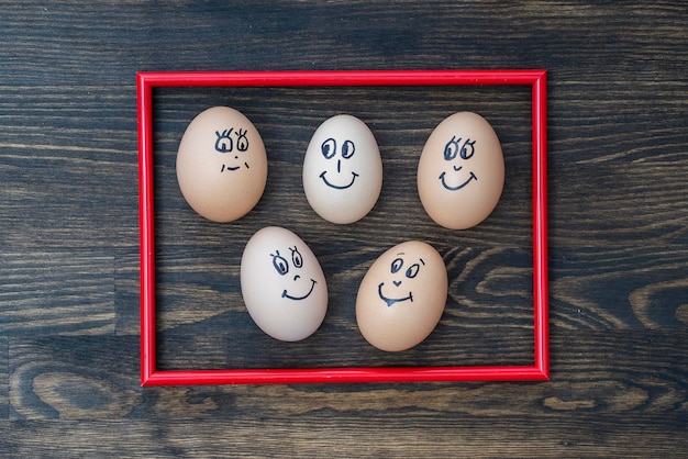 Picture red frame and many funny eggs smiling on wooden wall\
background closeup eggs family emotion face portrait concept funny\
food