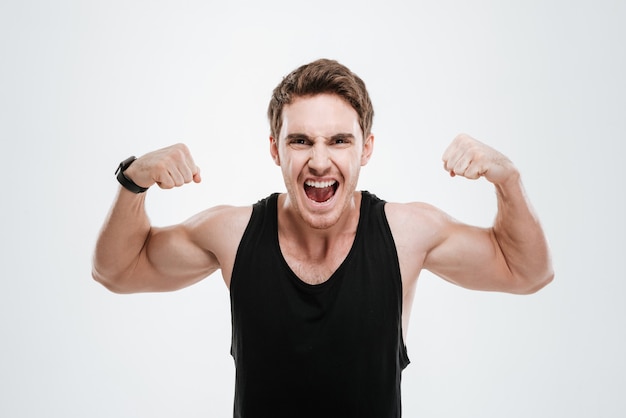Picture of screaming young man dressed in black t-shirt standing over white wall showing his biceps.