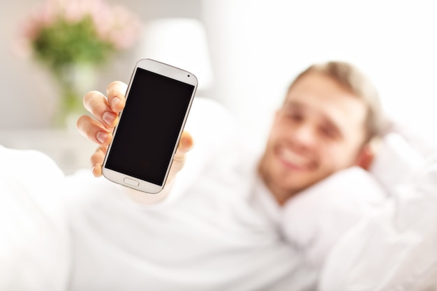 Picture showing handsome man lying in bed with smartphone