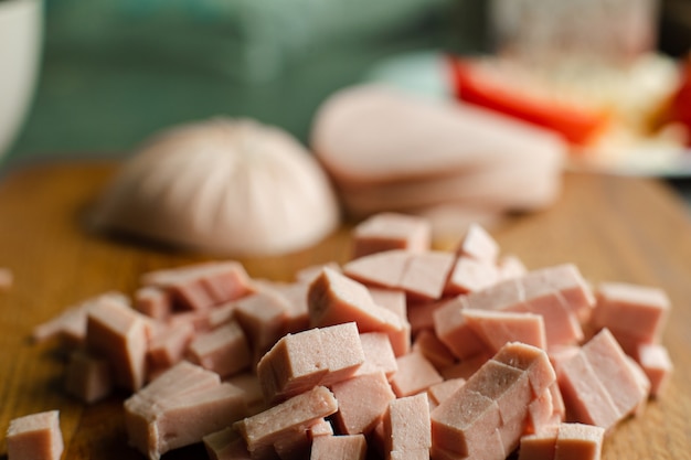 Изображение небольшой стопки нарезанной кубиками колбасы для приготовления на деревянном столе на кухне