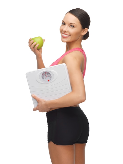 リンゴと体重計を持つスポーティな女性の写真