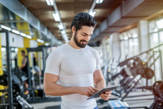 picture of strong handsome personal fitness trainer posing in front of the camera in bright gym.