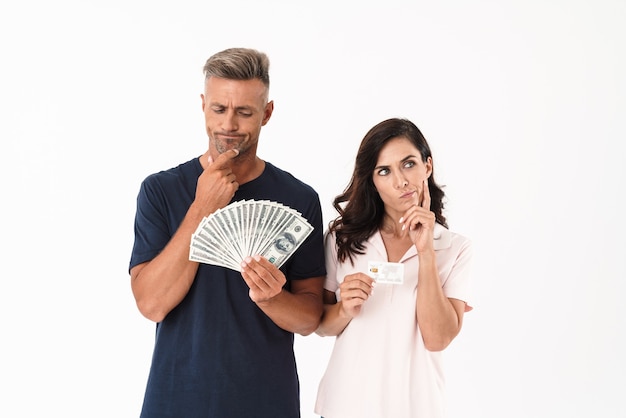 Photo picture of thinking serious adult loving couple isolated over white wall holding money and credit card.