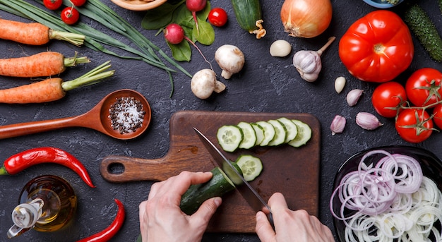 Picture on top of fresh vegetables, mushrooms, cutting board, oil, knife, hands of cook