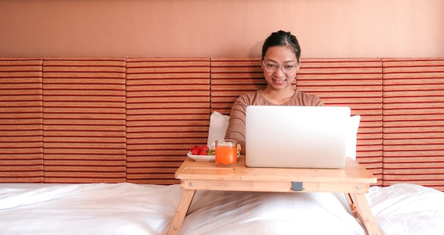 Picture of tourists used laptop and eating fruits on the bed in the luxury hotel room, healthy food concept.