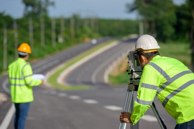 Picture of two civil engineers using theodolites measuring land coordinates standing at outdoor theodolites at a road construction site.