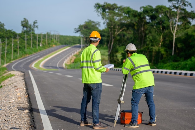 道路建設現場の屋外セオドライトに立っている土地座標を測定するセオドライトを使用している2人の土木技師の写真。