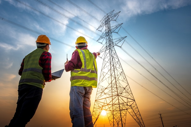 Picture of two electrical engineers checking electrical work using a computer standing at a power station to see the planning work at high voltage electrodes.