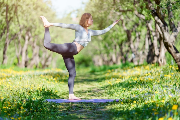 Picture of woman doing yoga standing on blue rug in forest on summer day
