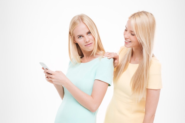 Picture of young attractive lady looking at the friend's phone. Isolated over white wall.