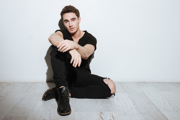 Picture of young attractive man dressed in black t-shirt sitting over white background and posing.